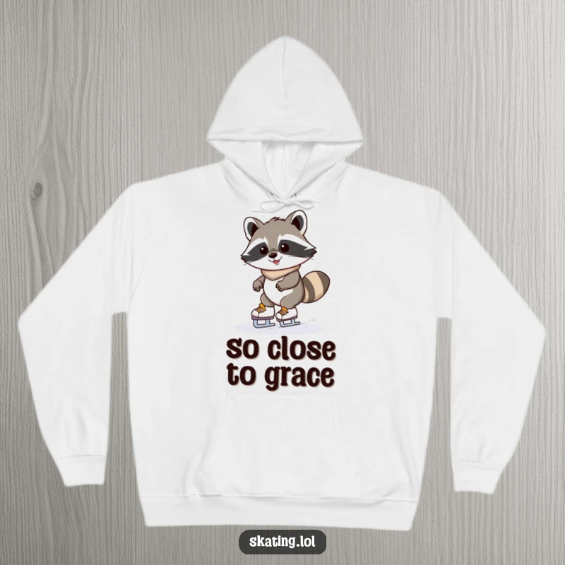 Funny raccoon hoodie with a determinedly grinning kawaii raccoon wobbling on ice skates; warm and humorous winter wear.